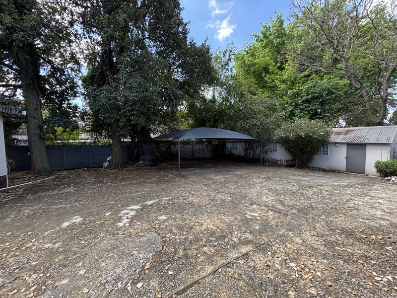 Spacious rear yard featuring extensive concrete paving, a shade sail structure, and a detached outbuilding with a corrugated metal roof.
