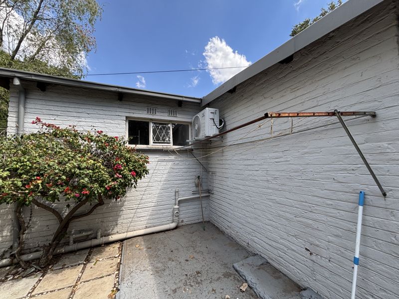 Rear exterior view of the cottage featuring painted brick walls, a wall-mounted clothesline, and an external air conditioning unit.