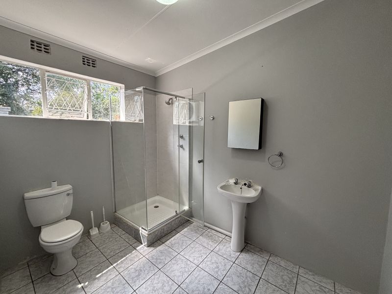 A clean and functional bathroom featuring a pedestal basin, a glass-enclosed shower, and tiled flooring with natural light from the window.