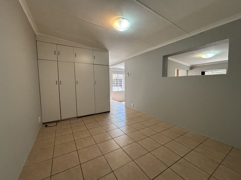 An empty bedroom featuring built-in cupboards, neutral wall paint, and ceramic floor tiles, with a unique interior wall cutout providing a view into the adjacent space.