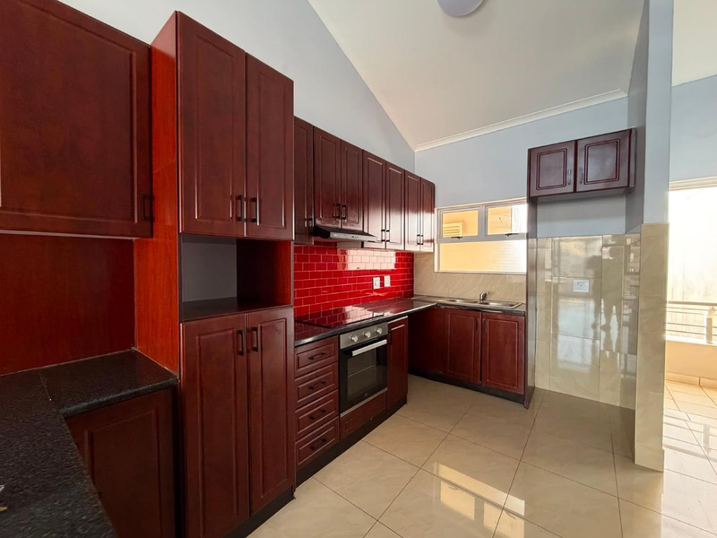 A clean, modern kitchen featuring dark wood cabinetry, granite countertops, a red tiled backsplash, and integrated stainless steel appliances.