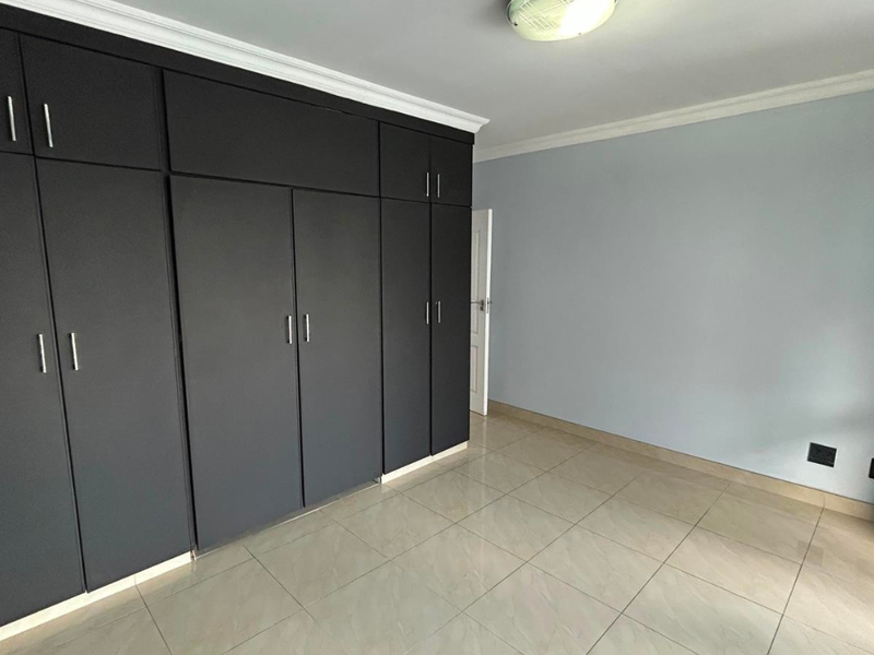 A clean, empty bedroom featuring modern dark built-in cupboards, neutral wall paint, and tiled flooring throughout.