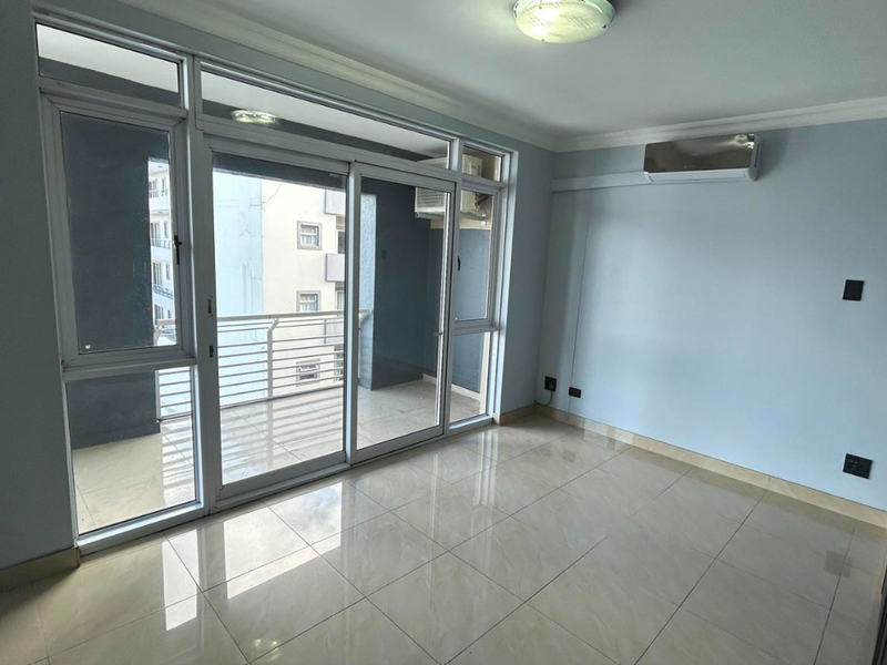 An empty, well-lit living area featuring polished tile floors, a split-system air conditioner, and large sliding glass doors leading to a private balcony.