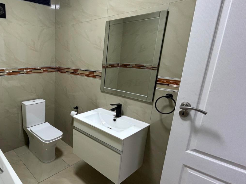 A modern bathroom featuring a wall-mounted vanity with a black mixer tap, a toilet, and neutral-toned wall and floor tiles.