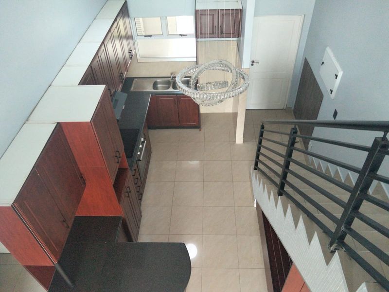 A high-angle view of a kitchen featuring dark wood cabinetry, tiled flooring, and an adjacent staircase with a modern metal railing.