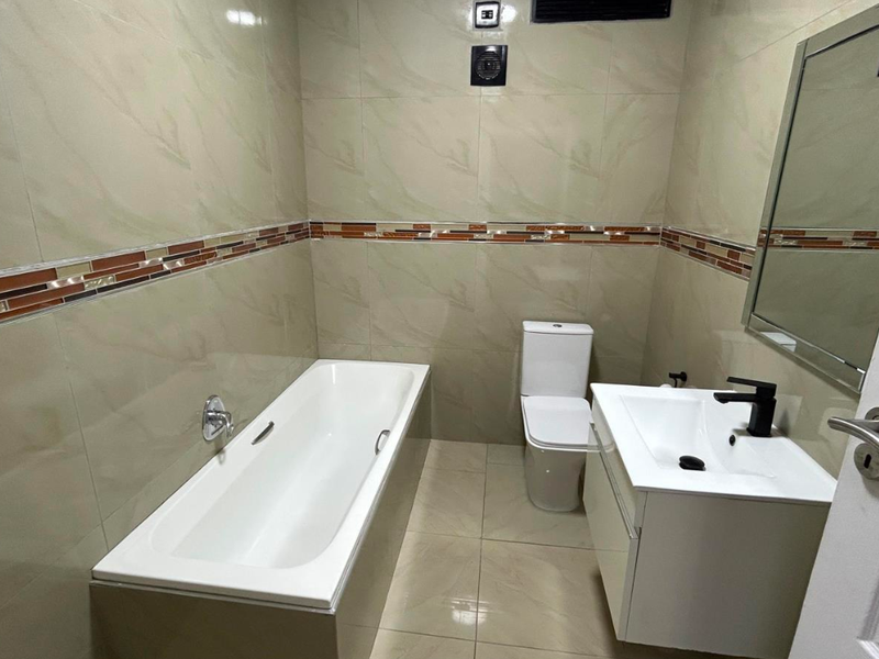 A clean, modern bathroom featuring a bathtub, a sleek vanity with a basin, and neutral wall tiling with a decorative accent border.