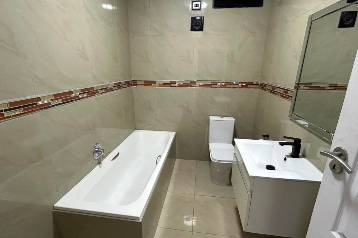 A clean, modern bathroom featuring a bathtub, a sleek vanity with a basin, and neutral wall tiling with a decorative accent border.
