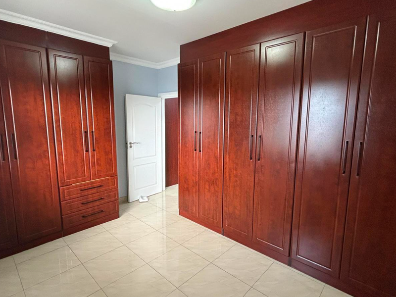 A spacious bedroom featuring extensive built-in wooden cabinetry, polished tile flooring, and neutral wall finishes.