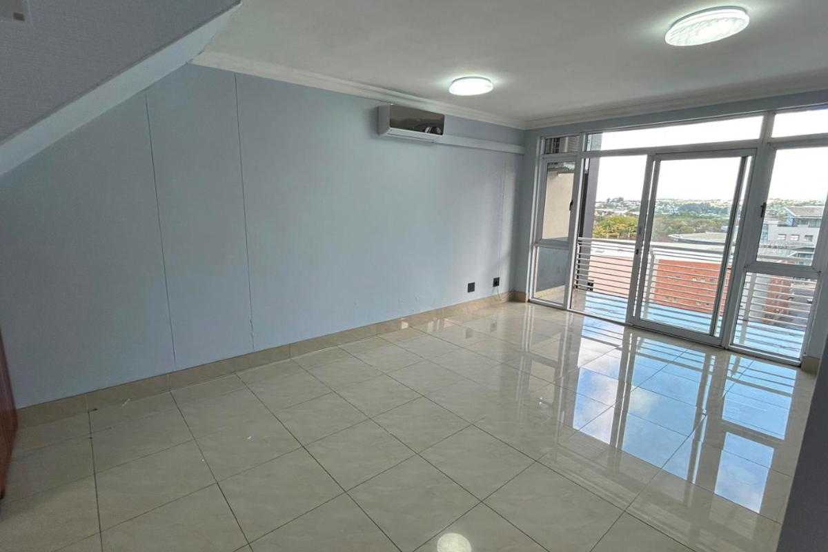 An empty, open-plan living area featuring polished tile flooring, a split-system air conditioner, and large sliding glass doors leading to a balcony.