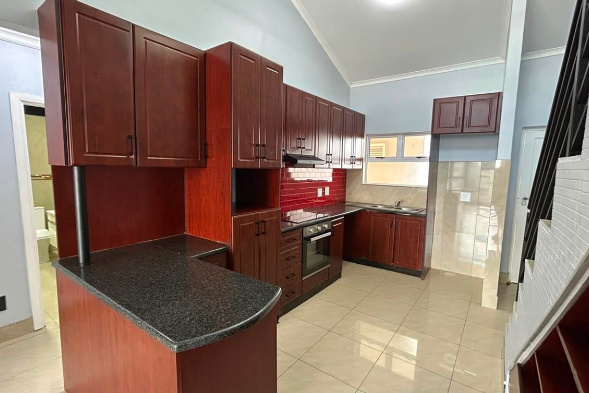 A spacious kitchen featuring dark wood cabinetry, granite countertops, built-in oven and hob, and tiled flooring under a vaulted ceiling.