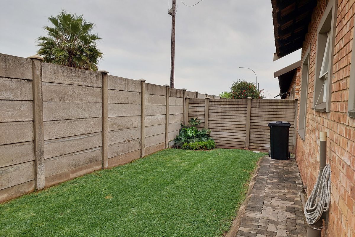 A private rear garden area featuring a lawn, brick paved pathway, and precast concrete boundary walling along the side of the townhouse.