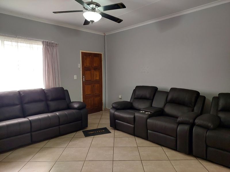 A living room featuring tiled flooring, a ceiling fan, and a wooden entrance door, providing a functional space with neutral wall tones.