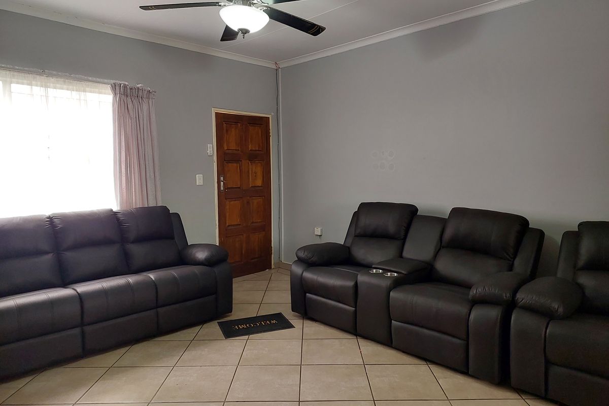 A living room featuring tiled flooring, a ceiling fan, and a wooden entrance door, providing a functional space with neutral wall tones.