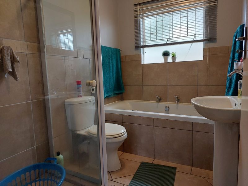 A functional bathroom featuring a bathtub, pedestal basin, toilet, and a glass-enclosed shower with neutral wall and floor tiling.