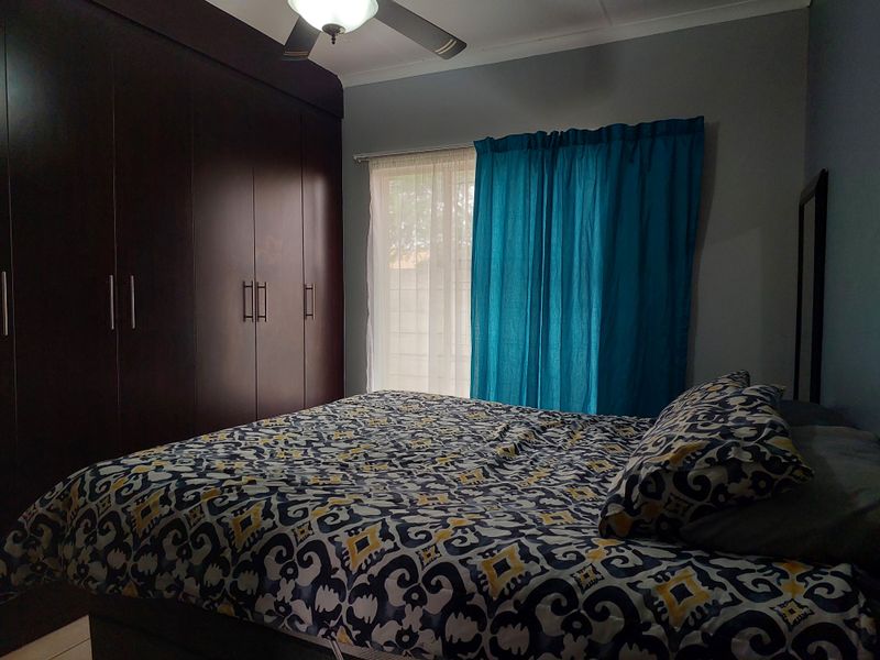 A bedroom featuring dark wood built-in cupboards and a ceiling fan, providing functional storage and climate control.