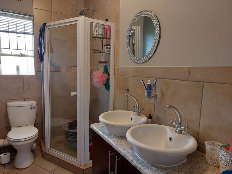 A functional bathroom featuring a dual vanity with basin sinks, a separate shower enclosure, and a toilet, finished with neutral wall tiling.