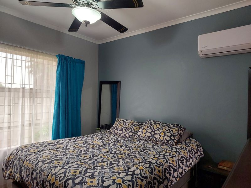A functional bedroom featuring a ceiling fan, wall-mounted split-system air conditioner, and security bars on the window.