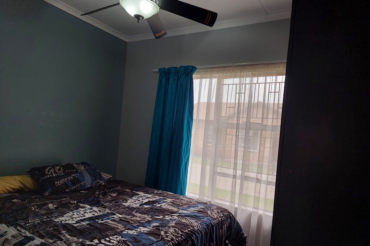 A bedroom featuring a ceiling fan, security bars on the window, and a built-in wardrobe.