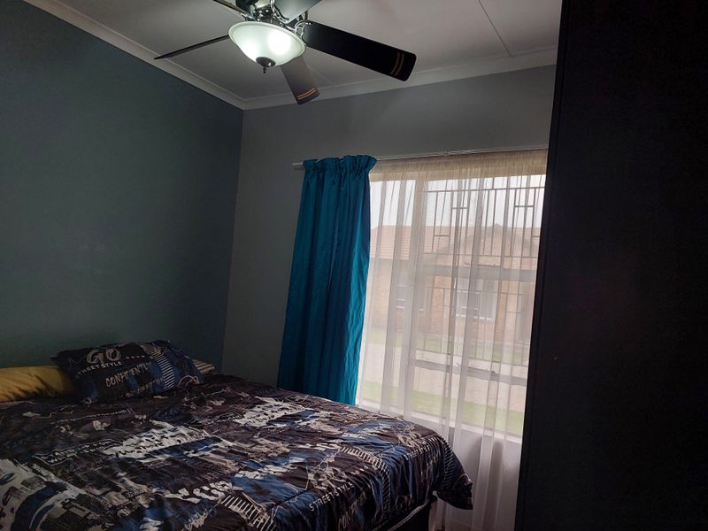 A bedroom featuring a ceiling fan, security bars on the window, and a built-in wardrobe.