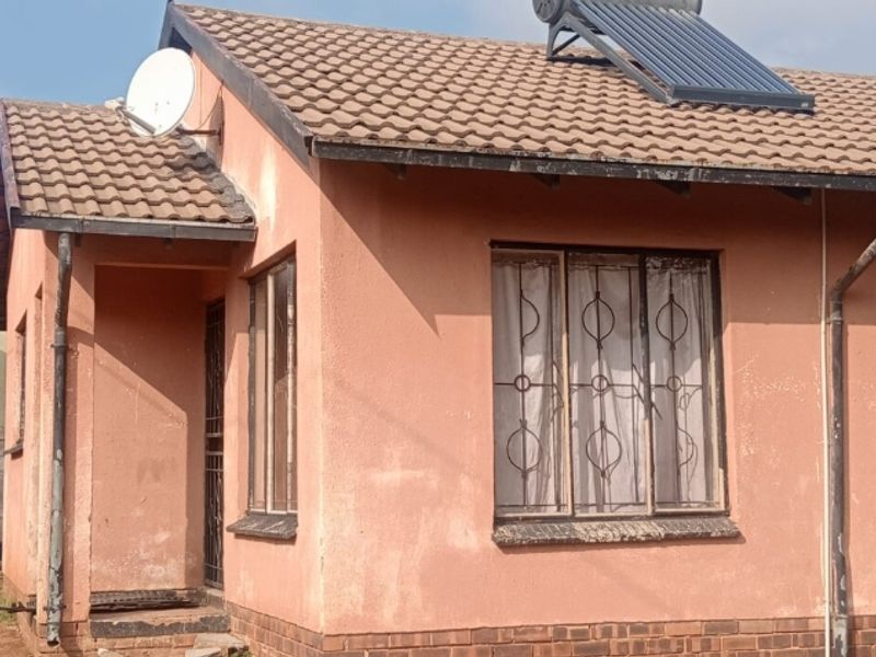 Front elevation of a single-story house featuring a tiled roof, solar water heating system, and security bars on the windows.