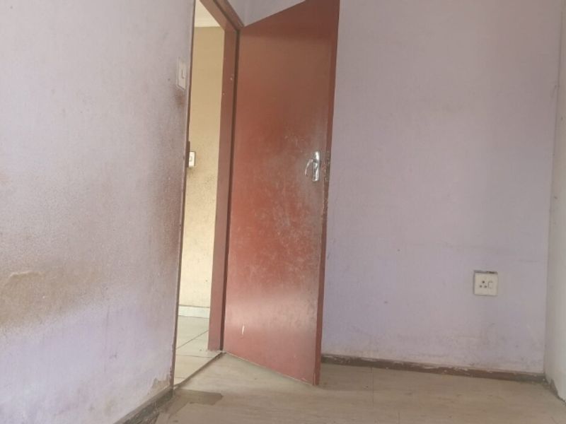 An empty bedroom interior featuring plain walls and a standard internal door, requiring cosmetic updates and fresh paint to improve its overall condition.