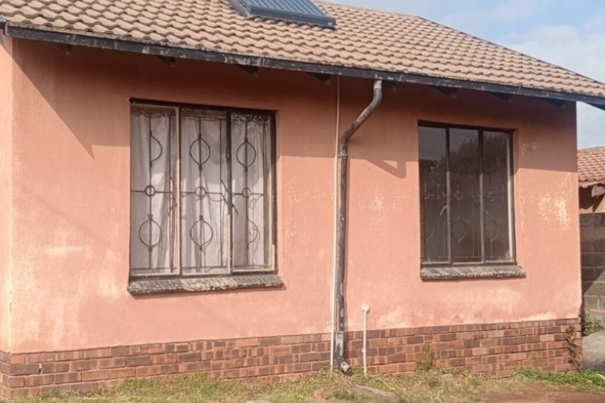 Exterior view of the house featuring a tiled roof with solar water heater, security bars on windows, and a brick plinth base.