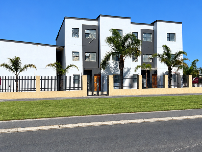 A modern three-story apartment building featuring a clean white and grey facade, secure perimeter fencing, and well-maintained landscaping.