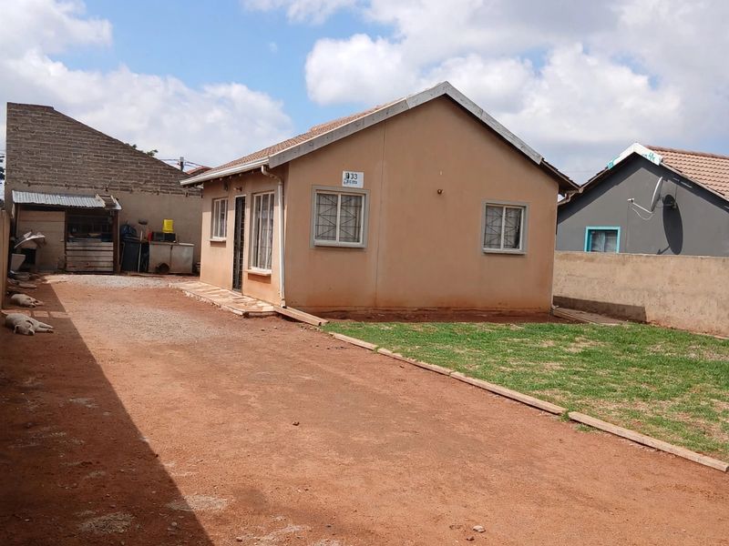 A detached single-story house featuring a tiled roof, security bars on windows, and a large unpaved yard area.