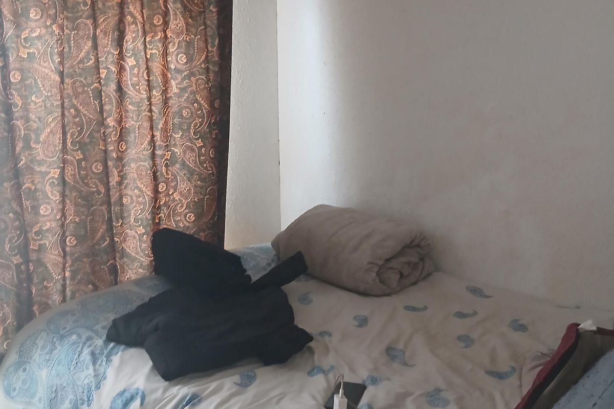 A compact bedroom featuring tiled flooring and a window with a curtain rod, requiring cosmetic updates to the wall finishes.