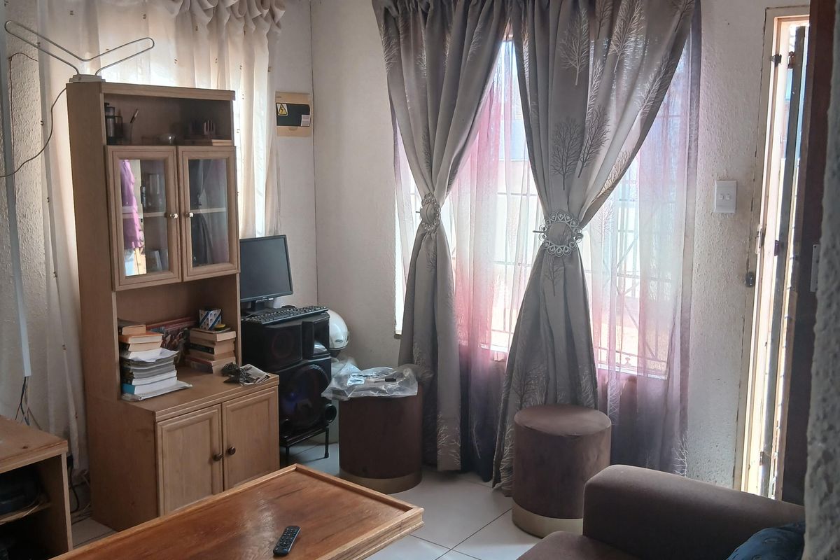 A compact living room featuring tiled flooring and recessed ceiling lighting, currently showing signs of wear on the wall surfaces.