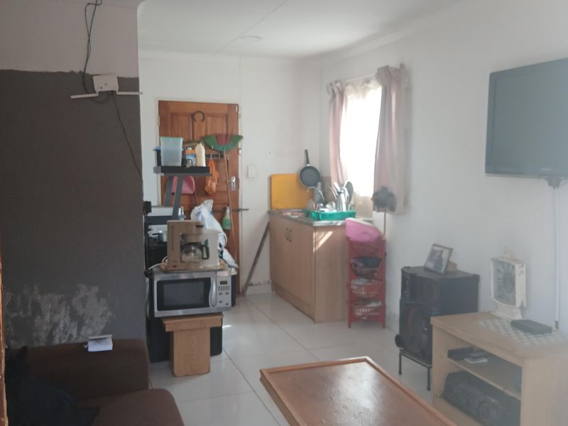 Open plan living area featuring tiled floors and a compact kitchen corner with cabinetry, requiring some cosmetic wall repairs and electrical tidying.