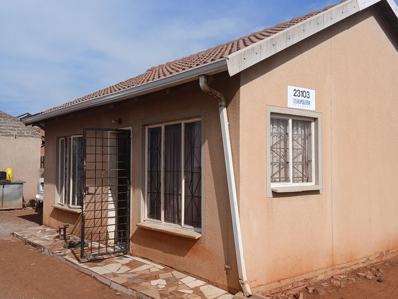 Exterior view of a single-story house featuring a tiled roof, security gates, and burglar bars, with visible wear on the exterior wall finish.