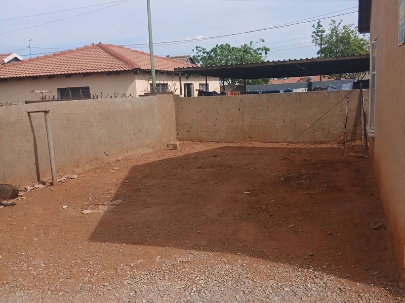 A rear exterior area featuring a concrete boundary wall, satellite dish, and an unpaved ground surface, offering potential for landscaping or outdoor development.