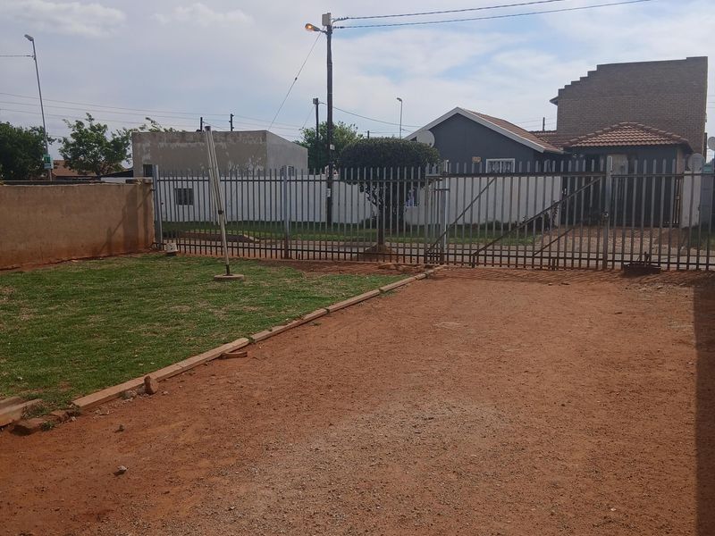 Front exterior view of the property featuring a gravel driveway, a small lawn area, and secure metal palisade fencing with a sliding gate.