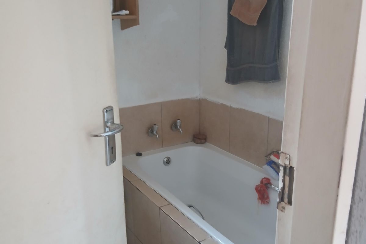 A compact bathroom featuring a built-in bathtub with tiled surround and splashback, offering a functional space in need of cosmetic updates.