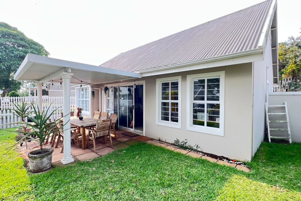 Rear view of the house featuring a covered patio area, sliding glass doors, and a well-maintained garden with a white picket fence.