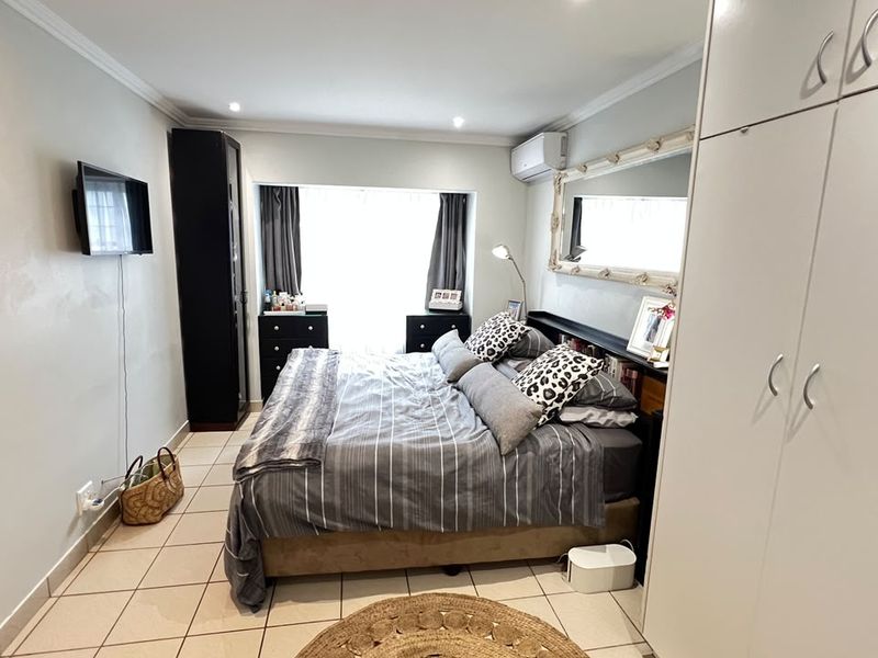 A well-maintained bedroom featuring tiled flooring, built-in wardrobe storage, and a wall-mounted air conditioning unit.
