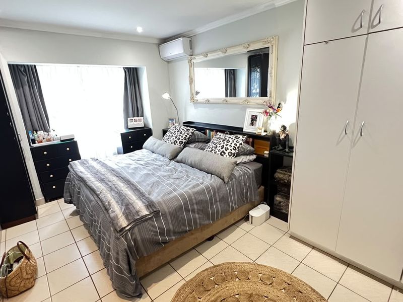 A well-maintained bedroom featuring tiled flooring, built-in cupboards, and a wall-mounted air conditioning unit.