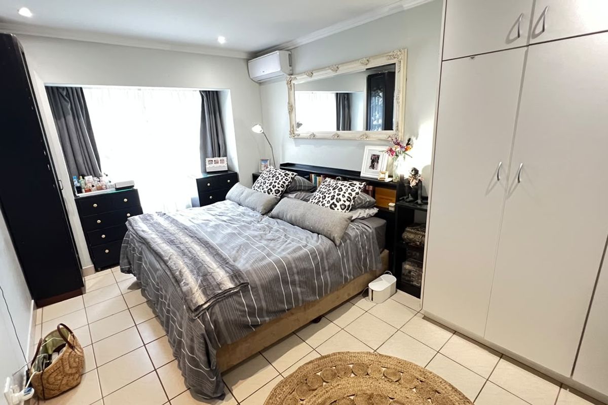 A well-maintained bedroom featuring tiled flooring, built-in cupboards, and a wall-mounted air conditioning unit.