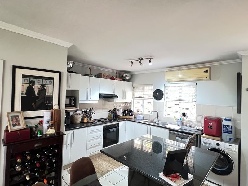 Functional kitchen featuring white cabinetry, granite countertops, integrated oven, and tiled flooring, with an adjacent laundry area and wall-mounted air conditioning unit.