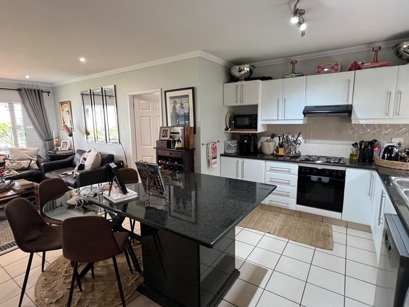 Open-plan living and kitchen area featuring a granite island, built-in appliances, tiled flooring, and direct access to an outdoor patio through sliding doors.