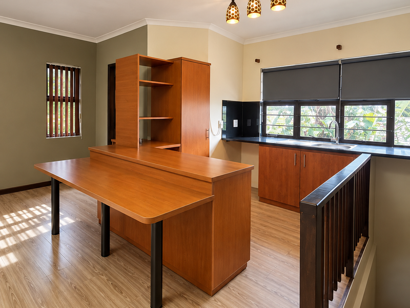 A bright, open-plan kitchen area featuring wood-toned cabinetry, a central island, laminate flooring, and a staircase with a wooden railing.