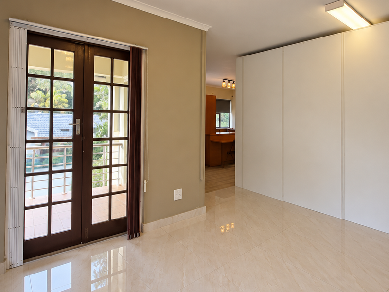 A bright, modern living area featuring polished tiled floors, built-in storage cupboards, and elegant lighting, with direct access to an outdoor balcony through french doors.