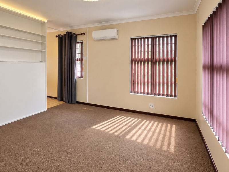 A bright, empty bedroom featuring neutral walls, carpet flooring, built-in shelving, and a split-system air conditioner.