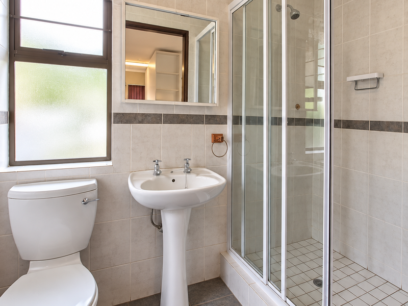 A functional bathroom featuring a pedestal washbasin, a toilet, and a glass-enclosed shower with tiled finishes throughout.