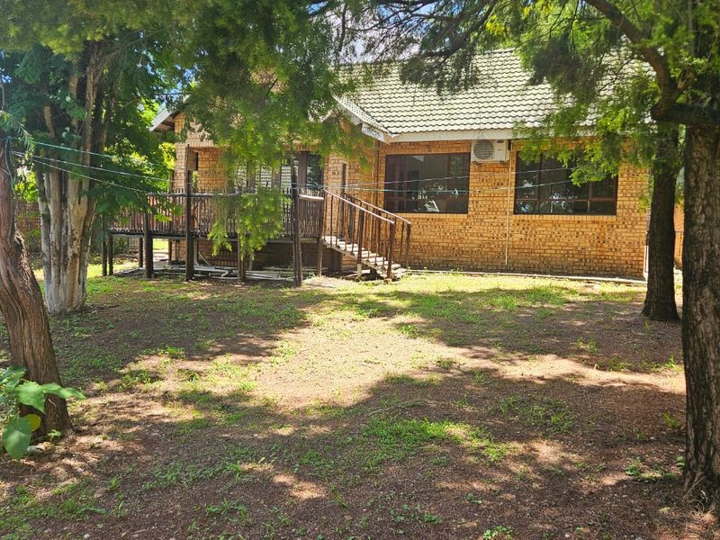 Rear view of a face brick house featuring a raised wooden deck, staircase, and a spacious garden area with perimeter walling.