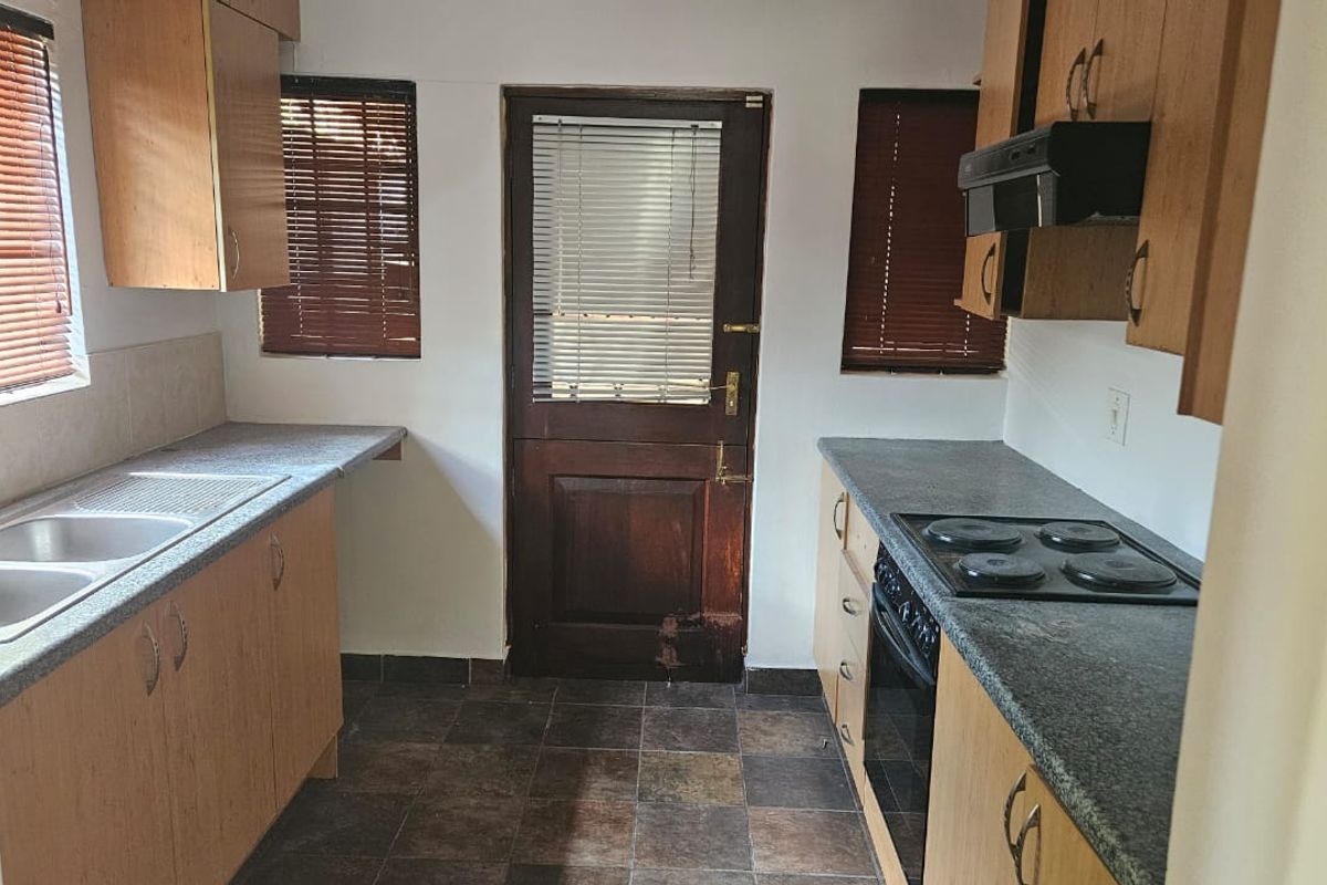A functional kitchen featuring laminate cabinetry, stone-look countertops, a double sink, and built-in electric cooking appliances with direct exterior access.