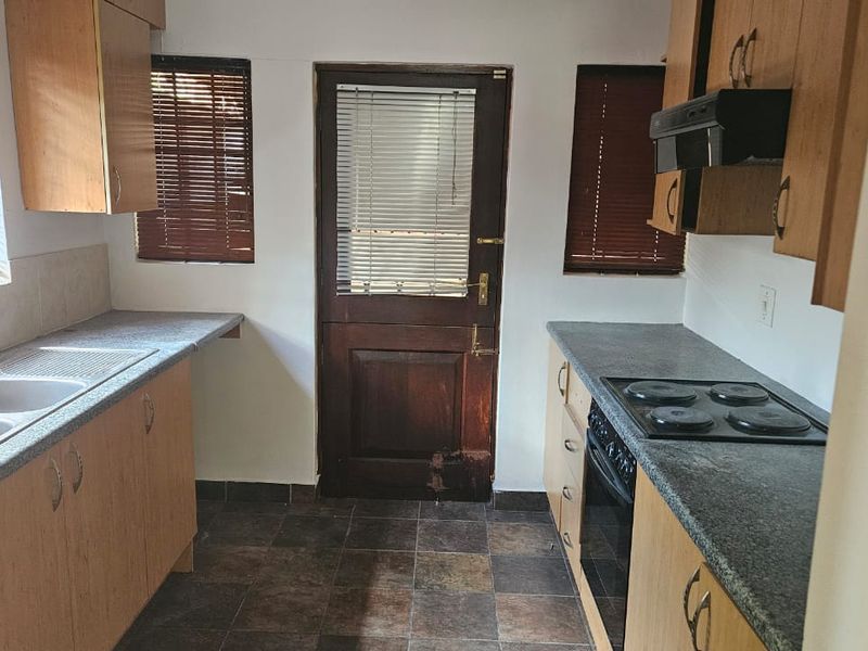 A functional kitchen featuring laminate cabinetry, stone-look countertops, a double sink, and built-in electric cooking appliances with direct exterior access.