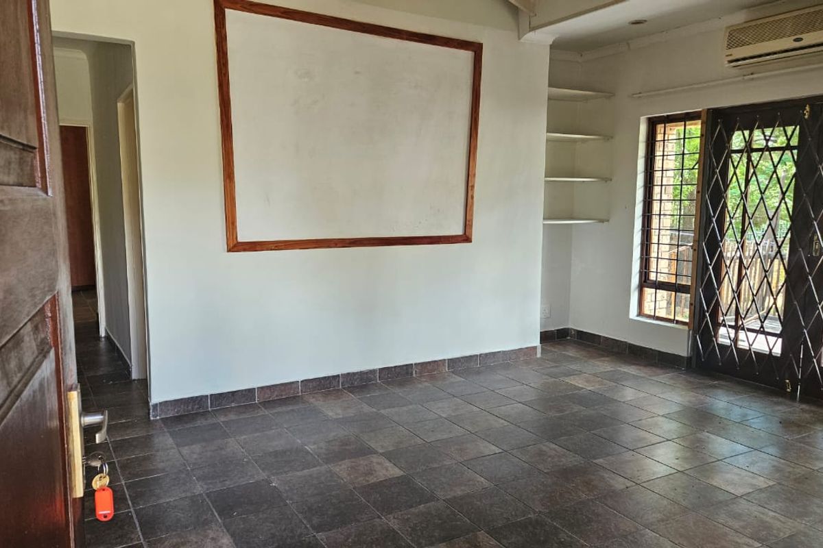 An empty living room featuring dark tiled flooring, built-in shelving, wall-mounted air conditioning, and security-gated french doors leading to an outdoor area.