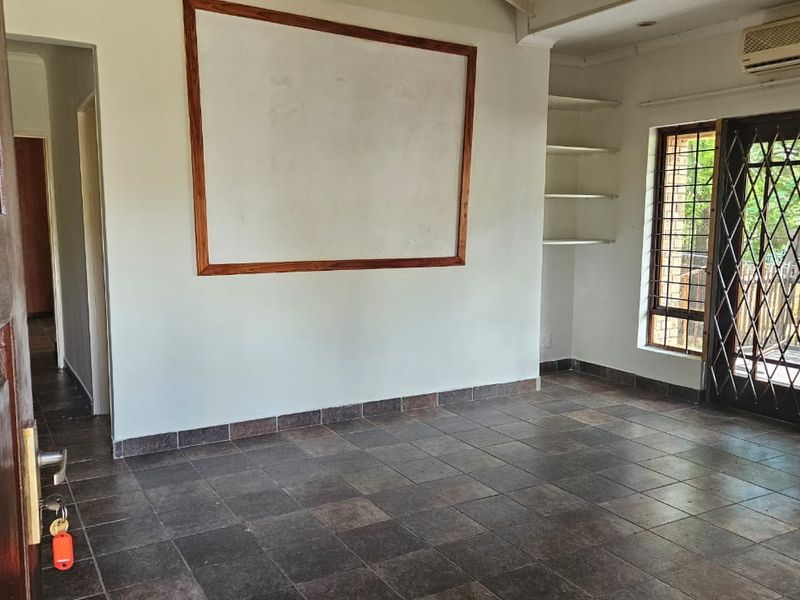 An empty living room featuring dark tiled flooring, built-in shelving, wall-mounted air conditioning, and security-gated french doors leading to an outdoor area.